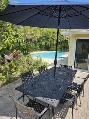 An outdoor patio with a pool table, chairs, and a large umbrella. - Thumb Point Oasis w/Heated Pool- walk to beach! (Fort Pierce)