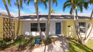 A yellow building with a blue door, surrounded by palm trees and a garden with a blue pot. - Thumb Point Oasis w/Heated Pool- walk to beach! (Fort Pierce)