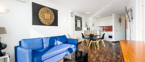 A living room with a blue sofa, a coffee table, and a dining area with chairs and a table.