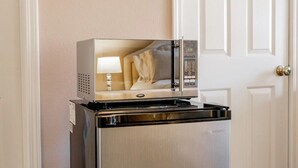Een compacte koelkast met een ingebouwde magnetron, in een gang met een witte deur en beige wanden.