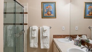 Een badkamer met twee wasbakken, een douchecabine met glazen wanden en twee handdoeken aan de muur.