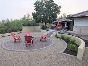 Un espace patio avec des fauteuils Adirondack rouges, un foyer et un coin salon couvert agrémenté d’un parasol rouge.