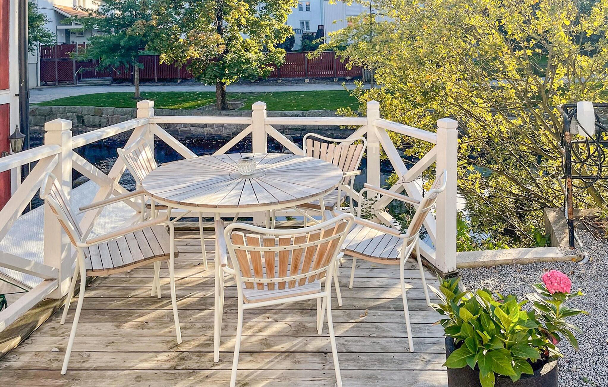 Une terrasse en bois avec une table ronde et des chaises blanches, entourée d’une clôture blanche.