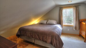 Ein Schlafzimmer mit schrägen Wänden, einem Bett mit brauner Bettdecke, einem Fenster mit Vorhängen und einem Holckindbett.
