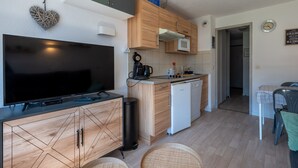 A compact living space with a flat-screen TV, wooden cabinetry, a kitchen area with a microwave, and a small dining area with a table and chairs. - Studio 4 ppl near the ski runs, family friendly (Morillon)