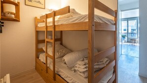 A bunk bed room with a wooden headboard, a bedside table with a lamp, and a view of the balcony. - Studio 4 ppl near the ski runs, family friendly (Morillon)