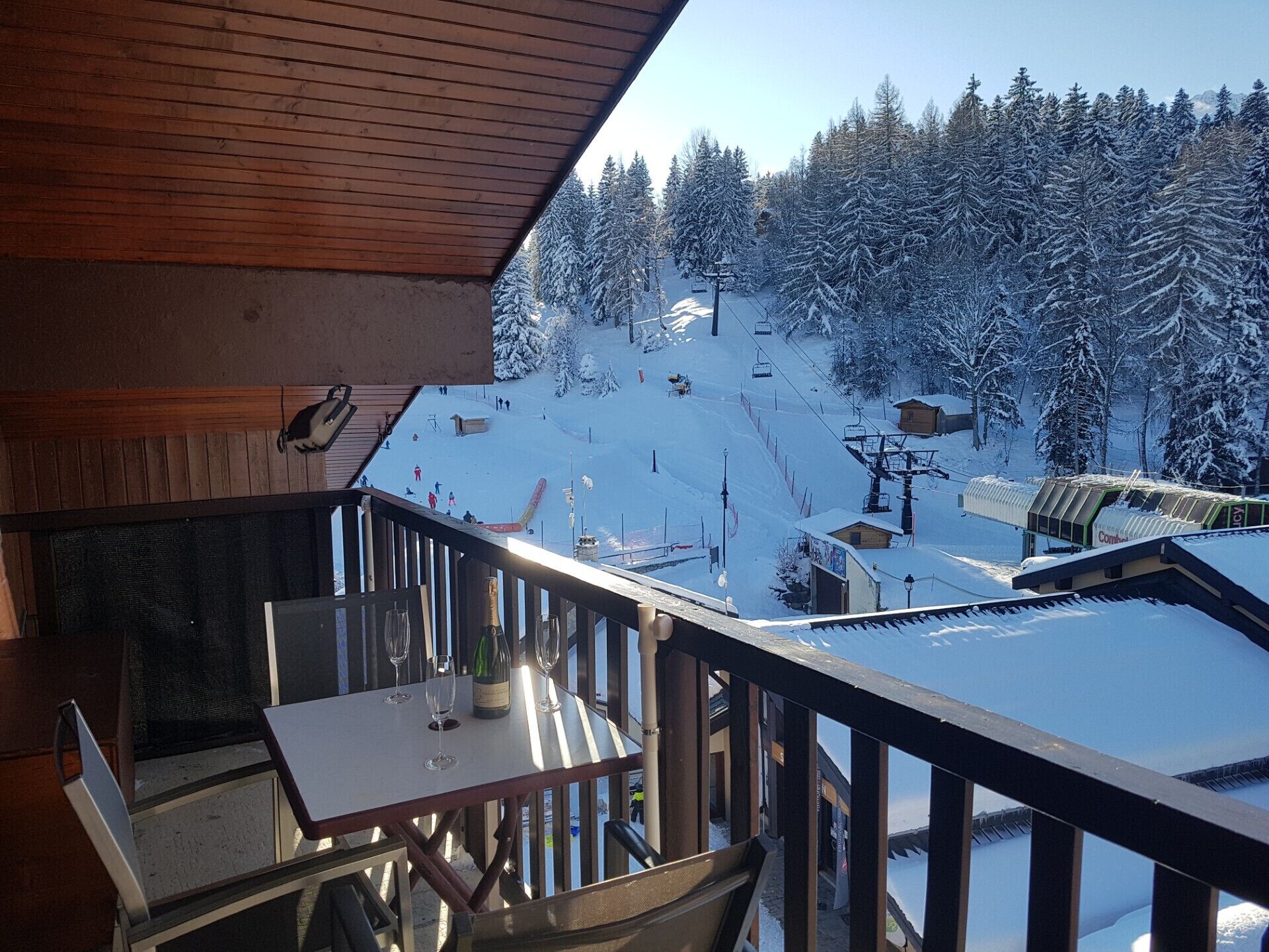 Balcón con mesa y sillas, con vistas a una pista de esquí nevada y un telesilla.