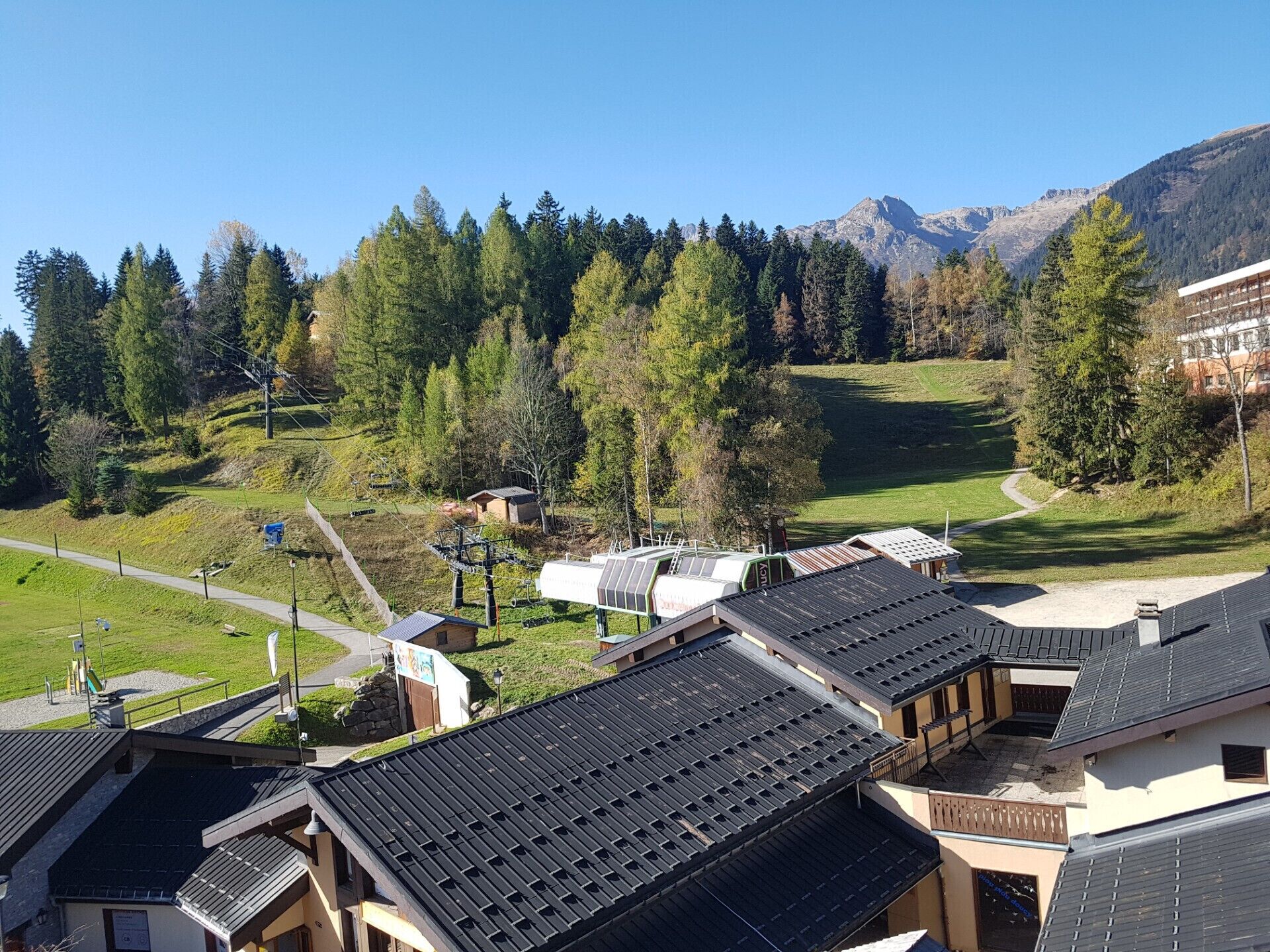A mountain resort with chalet-style buildings, a ski lift, and a view of the surrounding forest and mountains.