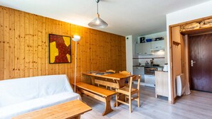 A cozy living room with a wooden wall, a dining table with benches, a sofa, and a kitchen in the background. - Cosy apt 6 ppl near the ski runs with balcony (Morillon)