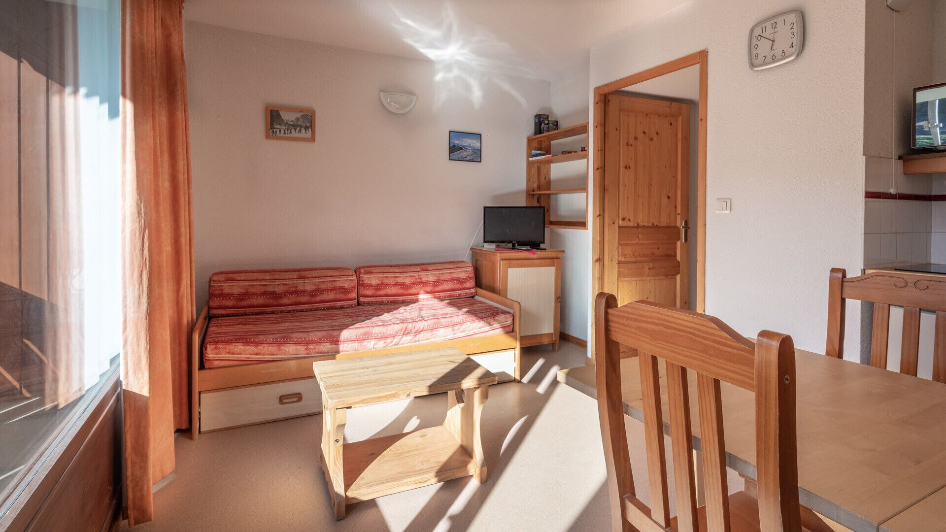 Une pièce chaleureuse avec un canapé en bois, une petite table en bois, un téléviseur posé sur un meuble et une porte en bois.