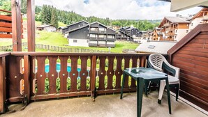 A balcony with a view of a mountain village, wooden buildings, and a pool.
