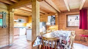 A wooden cabin interior with a kitchen, dining area, and a large window.