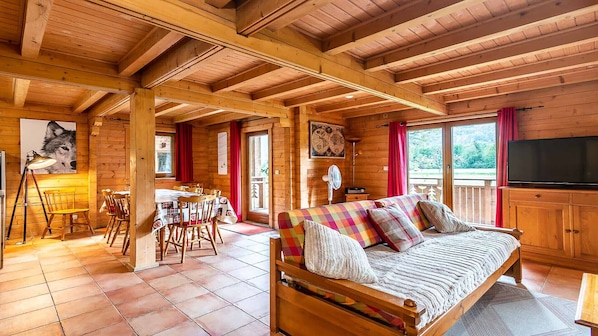A wooden cabin interior with a dining area, a sofa, and a television.