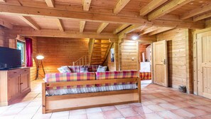 A wooden cabin interior with a bed, a desk, and a staircase leading to an upper level.