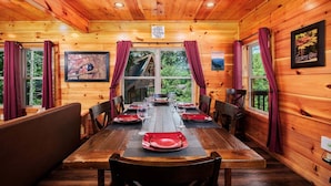 Ein Esszimmer in einer Holzhütte mit einem Tisch für sechs Personen, Vorhängen und gerahmten Bildern an den Wänden.