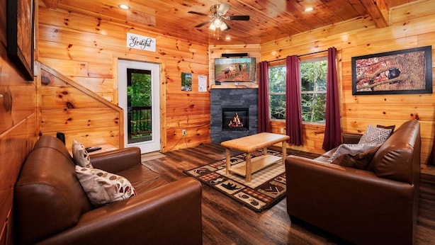 Ein gemütliches Blockhaushaus-Interieur mit Holzwänden, einem Kamin, Ledersofas und einem Deckenventilator.