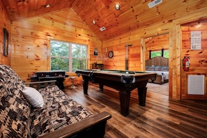 Interior de una cabaña de madera con mesa de billar, sofá y dardos.