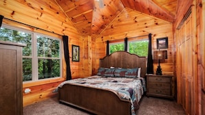 Ein Schlafzimmer einer Holzhütte mit Bett, Kommode und großen Fenstern.