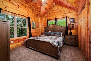 Un dormitorio de cabaña de madera con cama, cómoda y ventanas amplias.