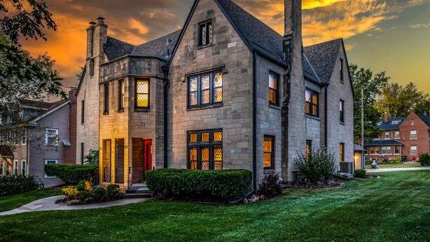 Une grande maison en pierre avec une porte rouge, plusieurs cheminées et une pelouse bien entretenue.