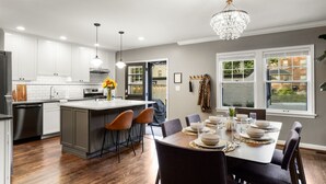 Une cuisine moderne avec des meubles blancs, un îlot central doté de tabourets et un coin repas avec une table dressée pour quatre personnes.