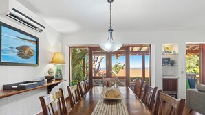 A dining area with a wooden table, chairs, a hanging light fixture, and a view of the outdoors. - Ocean View 4 Bedroom Villa Steps to Beach & Resort Amenities (Guanacaste Province)