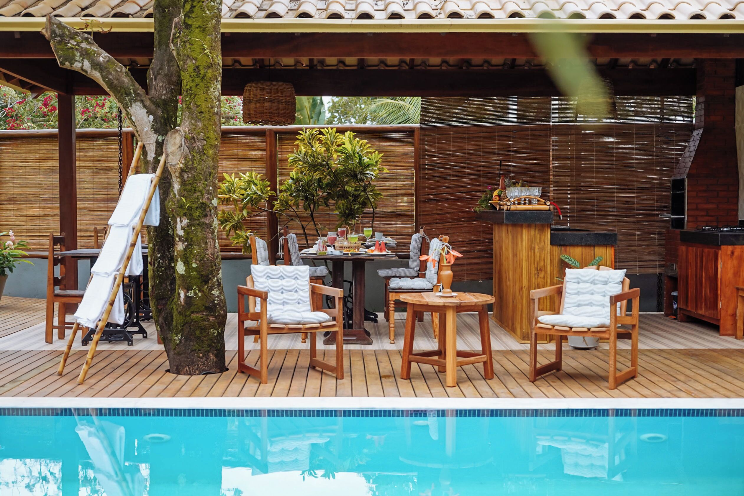 A poolside area with wooden deck, chairs, a table, and a hot tub.