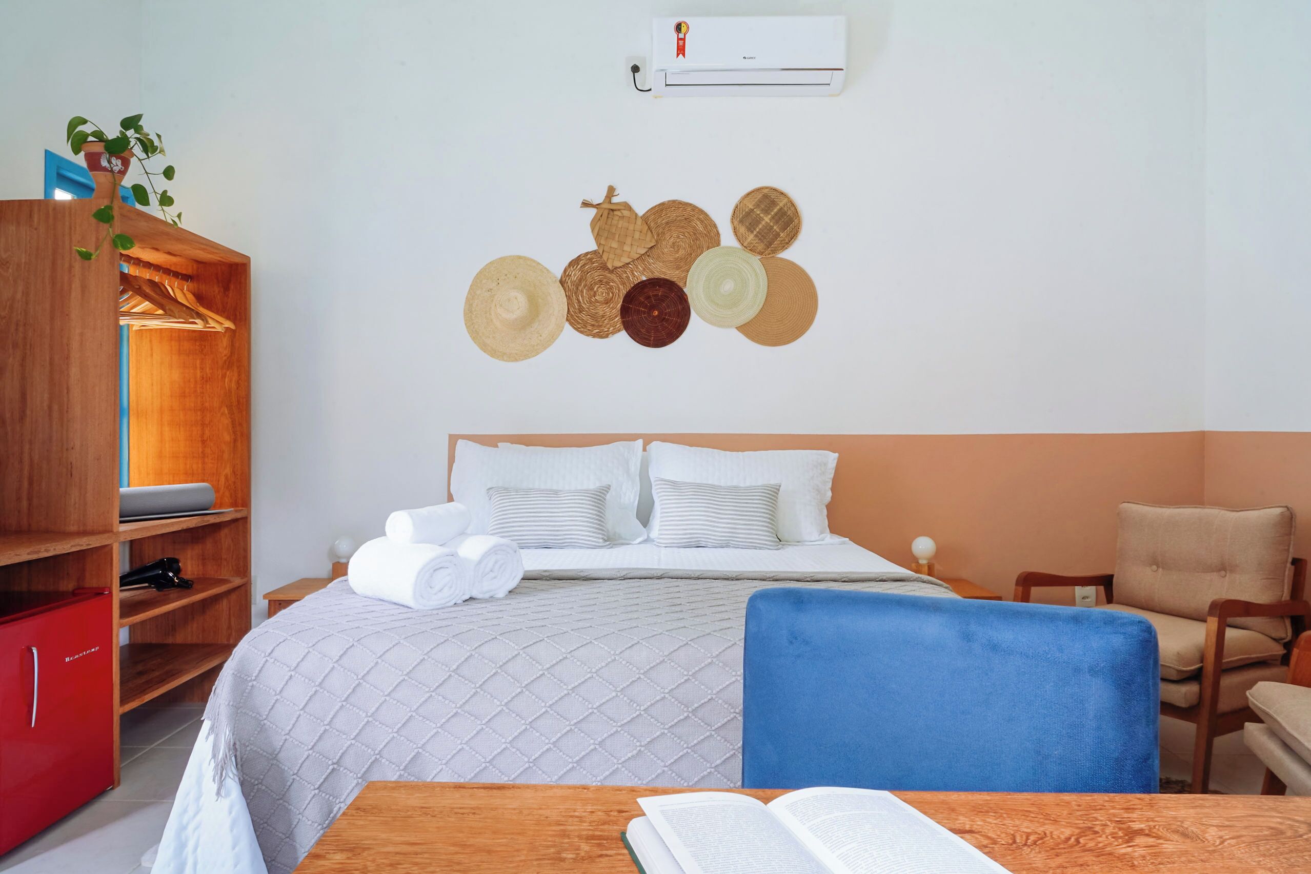 Habitación de hotel con cama, armario de madera, un mueble rojo, una silla azul y una pared decorada con platos.