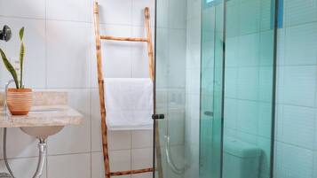 Un baño con cabina de ducha de vidrio, una escalera de madera, un lavamanos con un florero de plantas y una toalla blanca colgada en la pared.