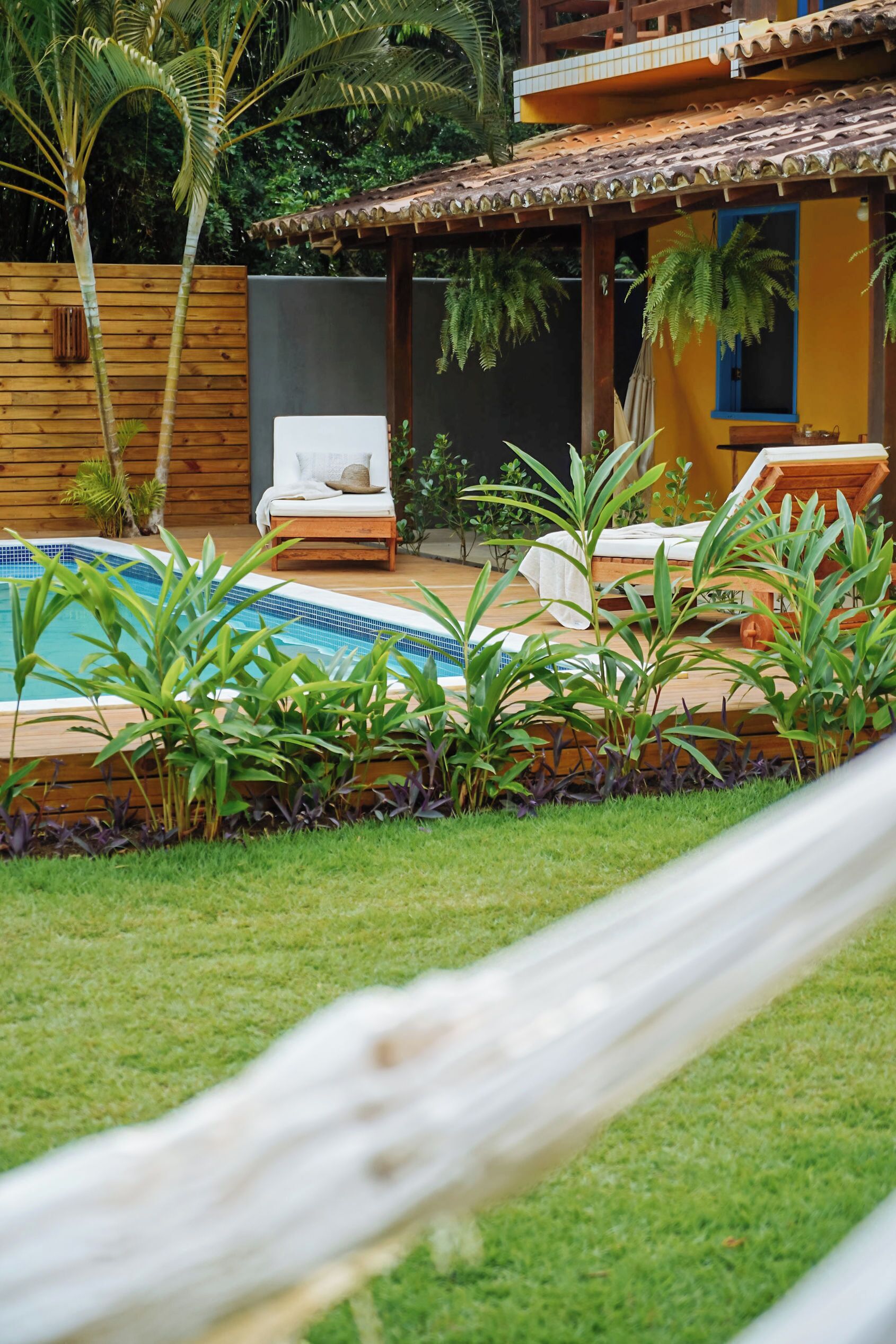 A pool area with lounge chairs, a hammock, and tropical plants.