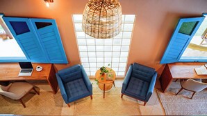 Una habitación con dos sillones azules, una mesa de madera con una planta y un ventanal con persianas.