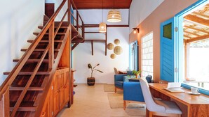 Una escalera de madera, una puerta azul, un escritorio con una silla y una lámpara colgante.