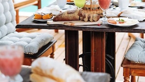 Zona de comedor junto a la piscina con una mesa dispuesta para el desayuno, incluyendo pan, frutas y bebidas.