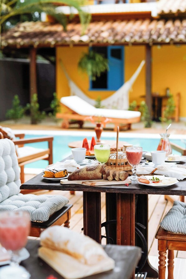 A poolside dining area with a table set for breakfast, including bread, fruits, and beverages.