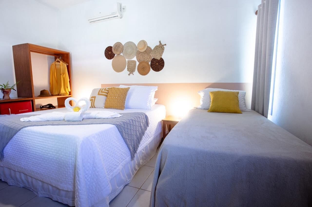 A hotel room with two beds, a wooden wardrobe, a wall-mounted decorative item, and a bedside table with a lamp.