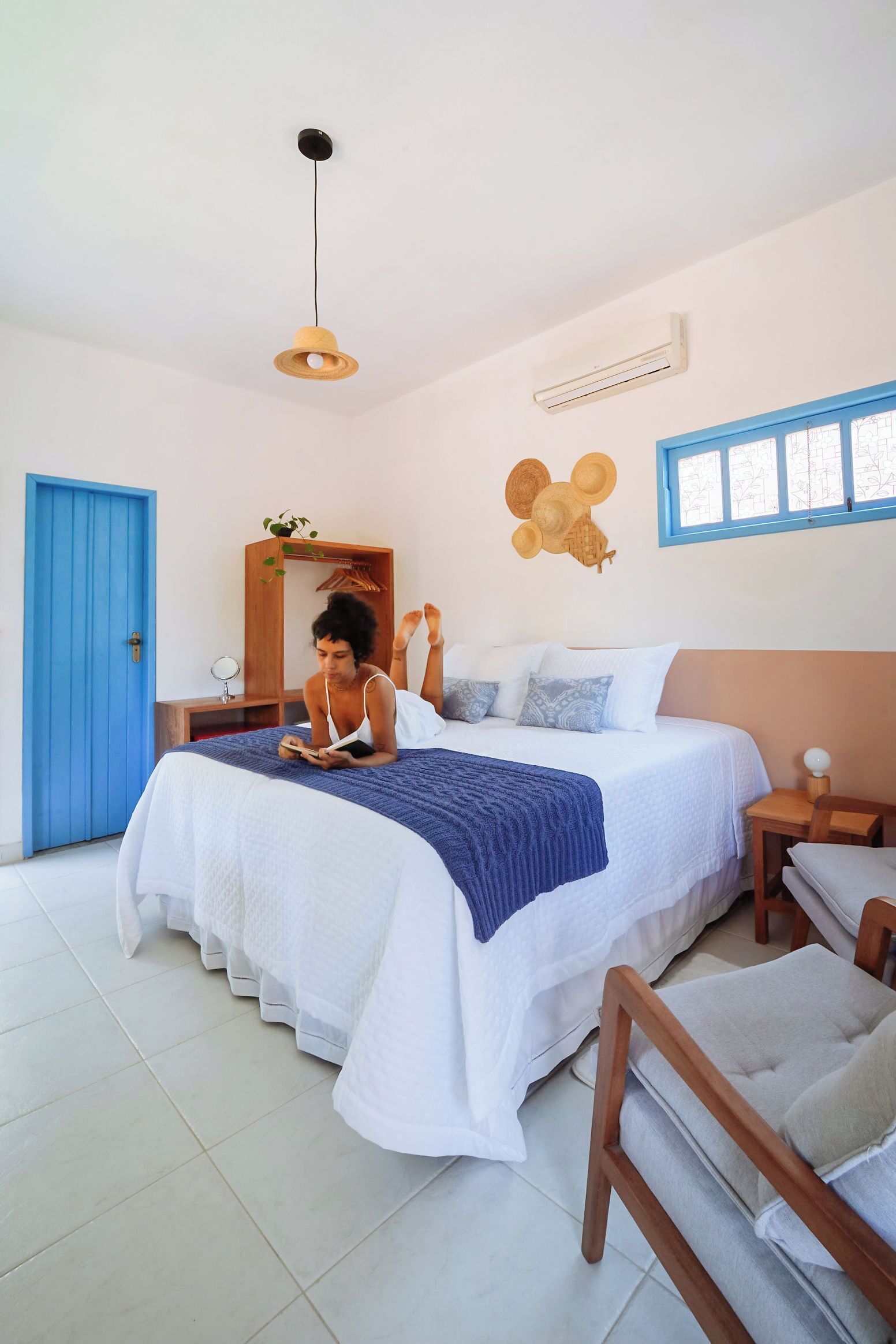 A bedroom with a bed, a bedside table, a mirror, a blue door, and a hanging light fixture.