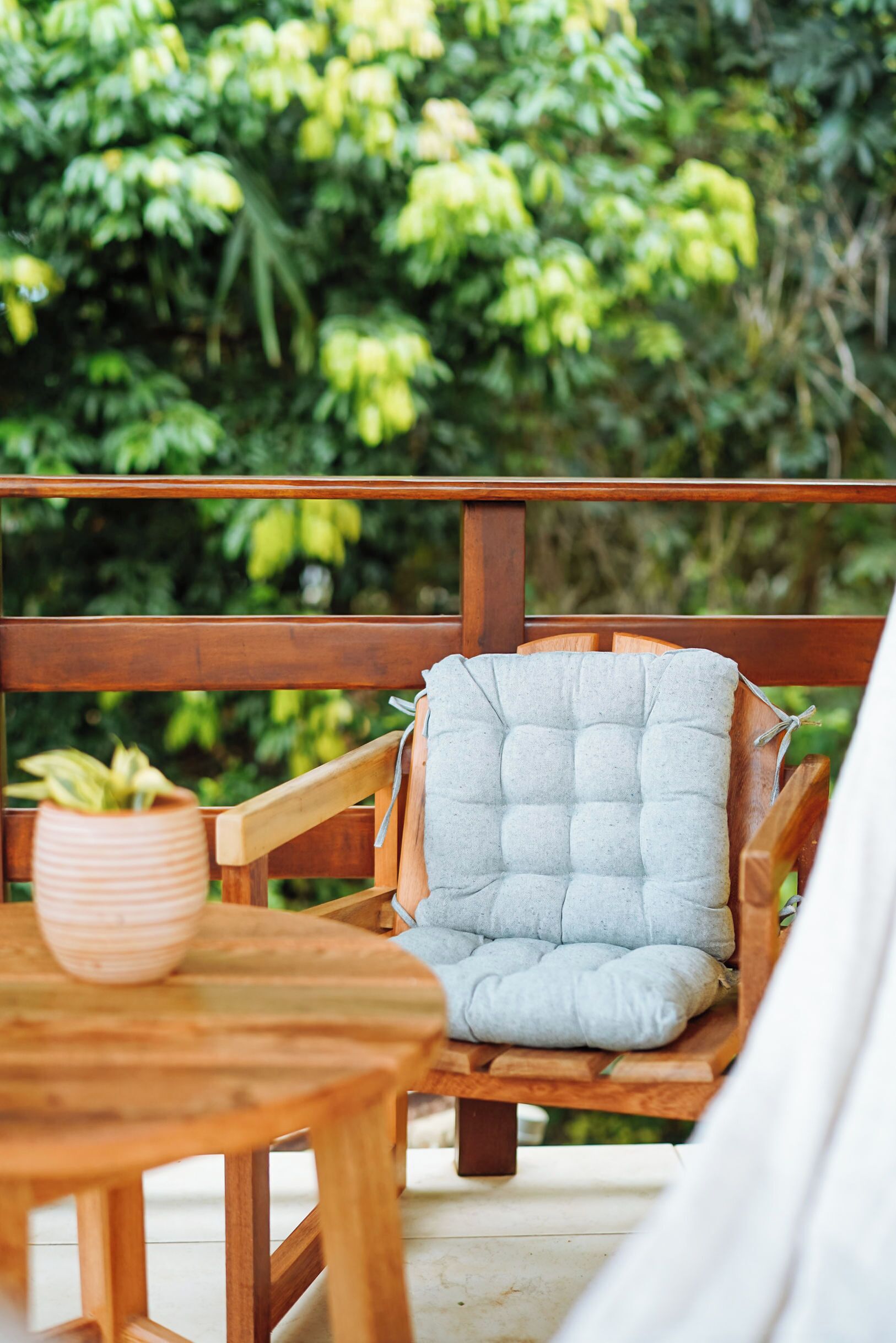 A wooden deck with a cushioned chair and a table with a potted plant.
