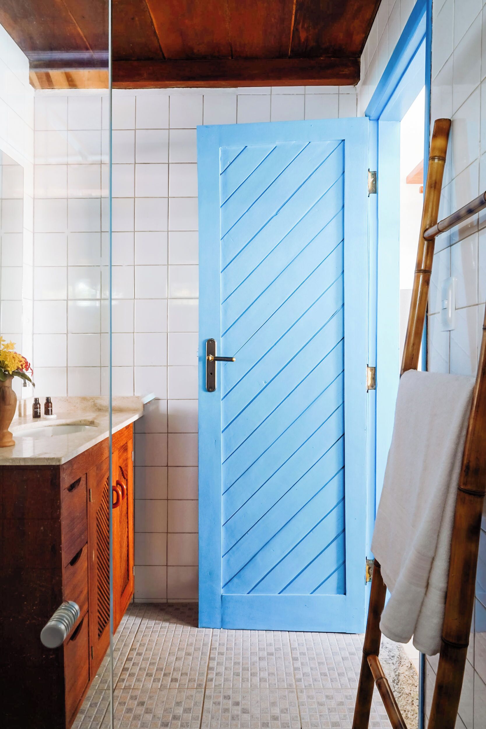 Un baño con puerta azul, armarios de madera, una escalera de bambú y suelo de baldosas.