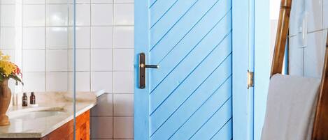 Un baño con puerta azul, armarios de madera, una escalera de bambú y suelo de baldosas.
