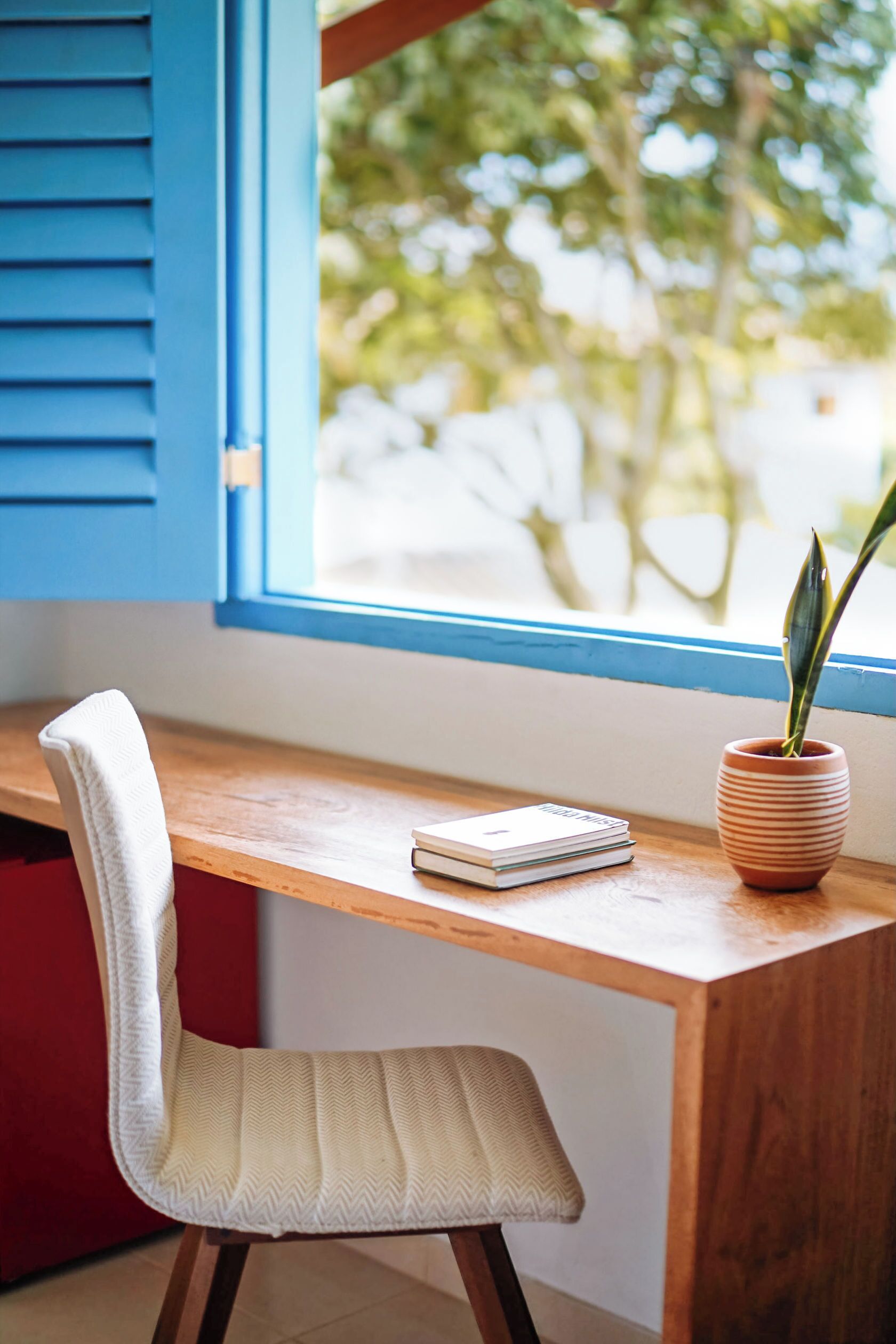 A wooden desk with a white chair, a potted plant, and a notebook.