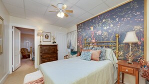 Une chambre à coucher comprenant un lit, une table de chevet, une commode et un ventilateur de plafond.