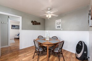 A dining room with a wooden table and chairs, a ceiling fan, and a wall-mounted heater.