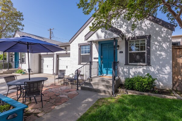 A house with a blue door, a patio with a table and chairs, and a small garden.