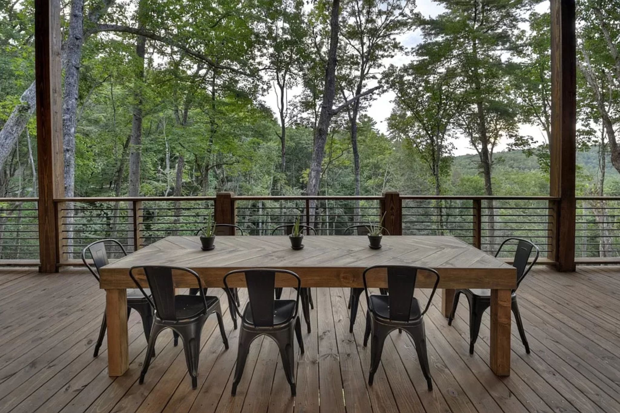 A wooden deck with a table and chairs, surrounded by a railing with a view of a forest.