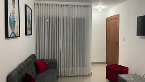 Una sala de estar moderna con un sofá gris, cojines rojos, un reposapiés rojo, una mesa de centro de vidrio y un televisor en la pared.