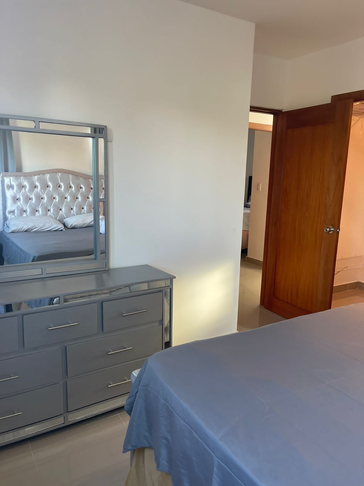 Un dormitorio con una cama, un aparador, un espejo y una puerta de madera.