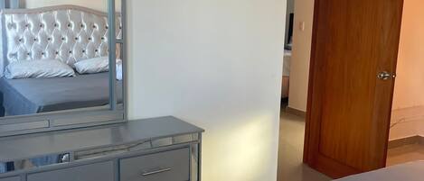 Un dormitorio con una cama, un aparador, un espejo y una puerta de madera.