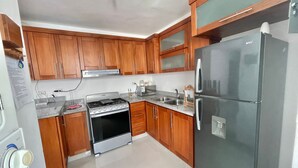 Una cocina con armarios de madera, estufa, refrigerador y pileta.