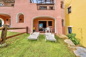 A pink building with a covered patio area featuring two lounge chairs and a table.