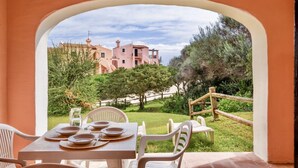 A dining area with a table set for four, overlooking a pink building and a garden with a wooden fence. - 60 sq m - Living room with kitchenette and double sofa bed, double bedroom, bathroom with bidet and showeror bathtub.<br>Ground floor with furnished veranda.<br>Equipped with:<br>- tv <br>- washing machine<br>- 1 beach umbrella<br>- iron and ironing boar (Stintino)